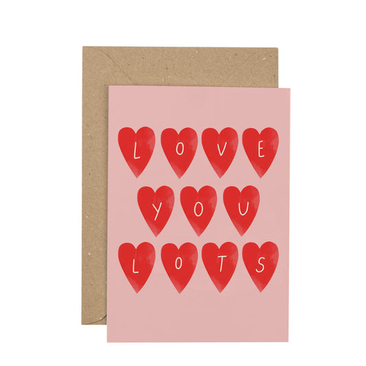 Greeting card with red hearts spelling 'I LOVE YOU LOTS' on a pink background, with a brown envelope.