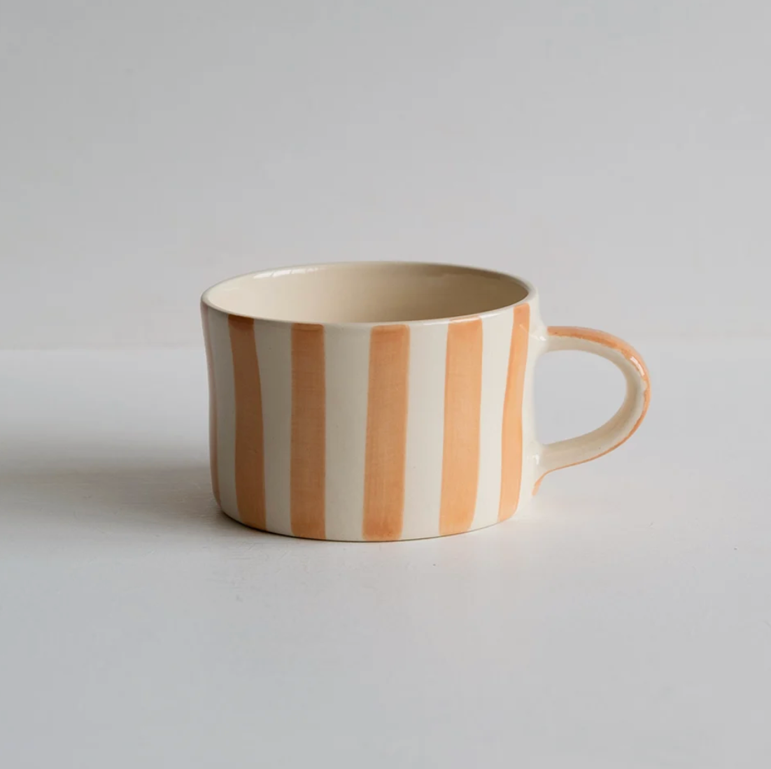 A ceramic coffee mug with vertical peach and cream stripes, featuring a small handle and a glossy finish, set against a plain light gray background.