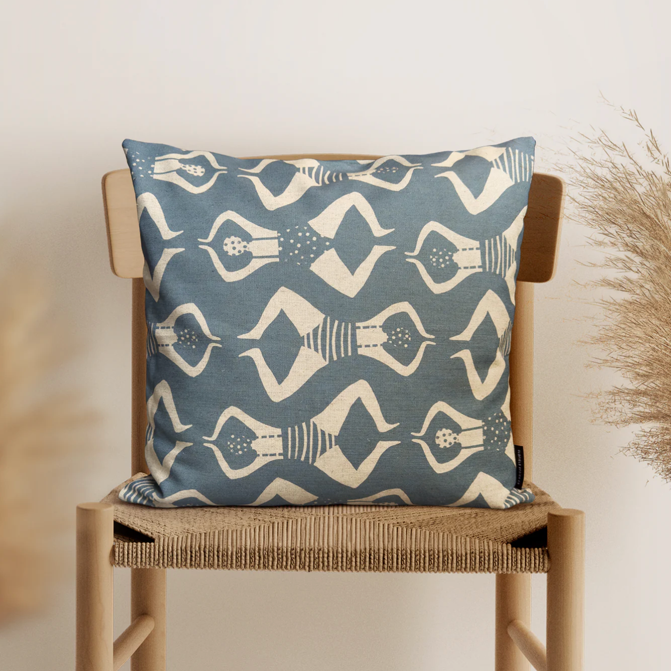 Blue pillow with white pattern on a wooden chair against a neutral background