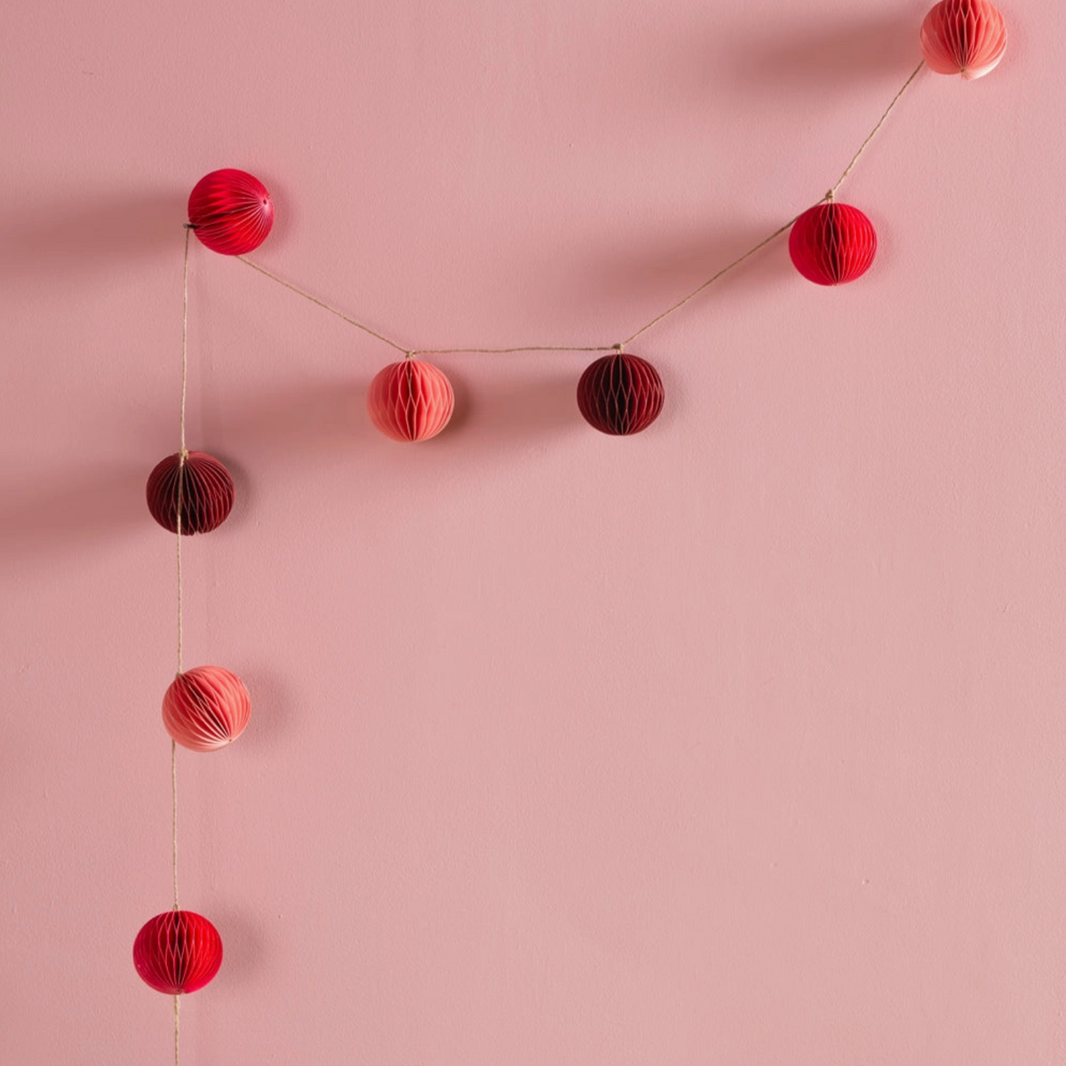 pink and red paper origami garland hung against a pink wall