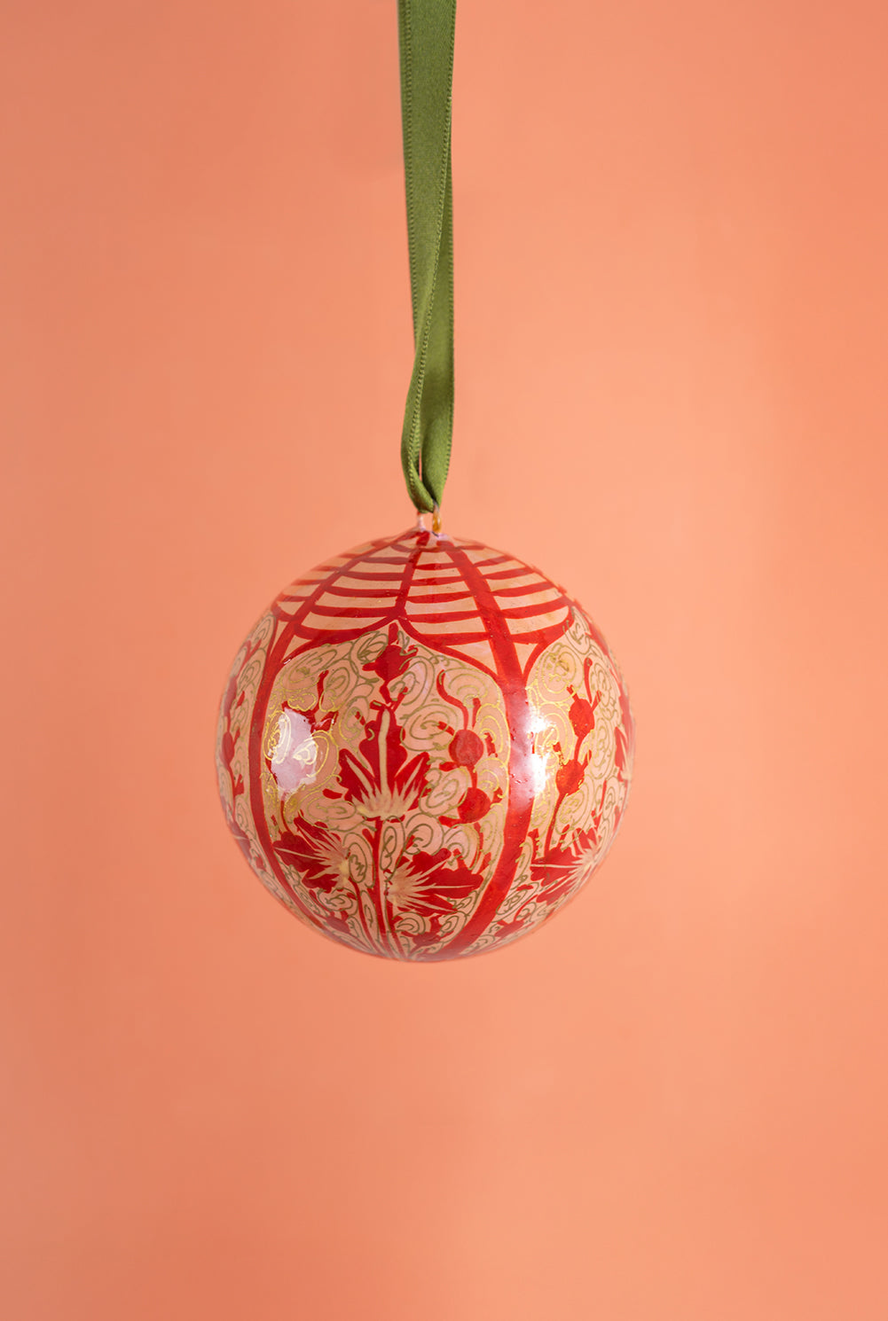 Decorative Christmas ball ornament with red and gold pattern on a peach background