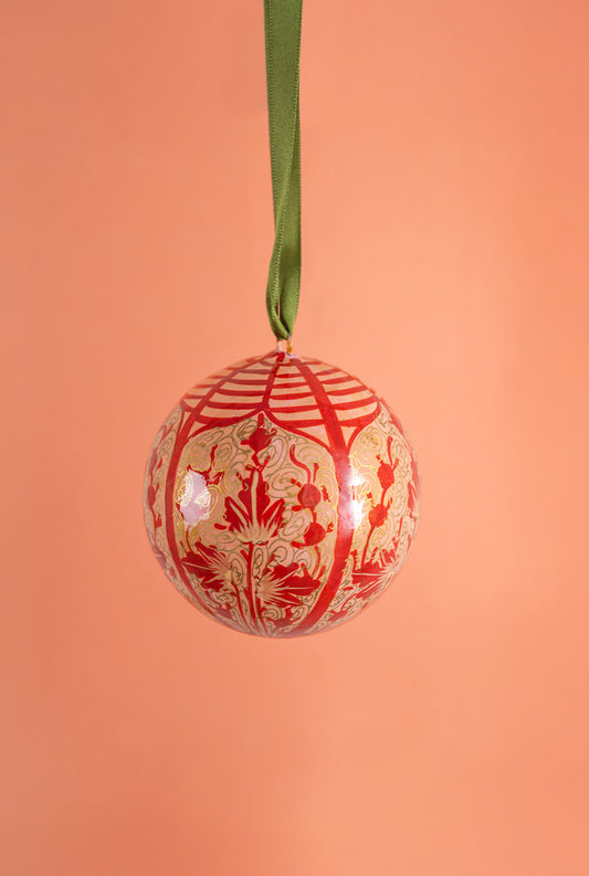Decorative Christmas ball ornament with red and gold pattern on a peach background