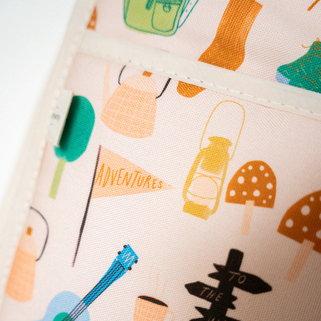 A close-up of a pair of plewsy double oven gloves featuring a whimsical, multicolor 'Adventure' print with illustrations of a blue guitar, green trees, orange mushrooms, and directional road signs on a light pink background.