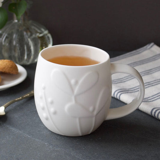 White mug with tea on a dark surface with cookies and a vase in the background