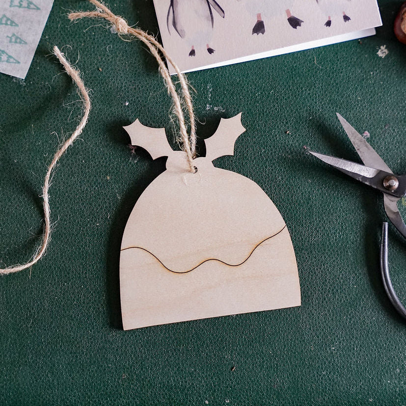 a wooden christmas pudding decoration on a green background, surrounded by crafting items