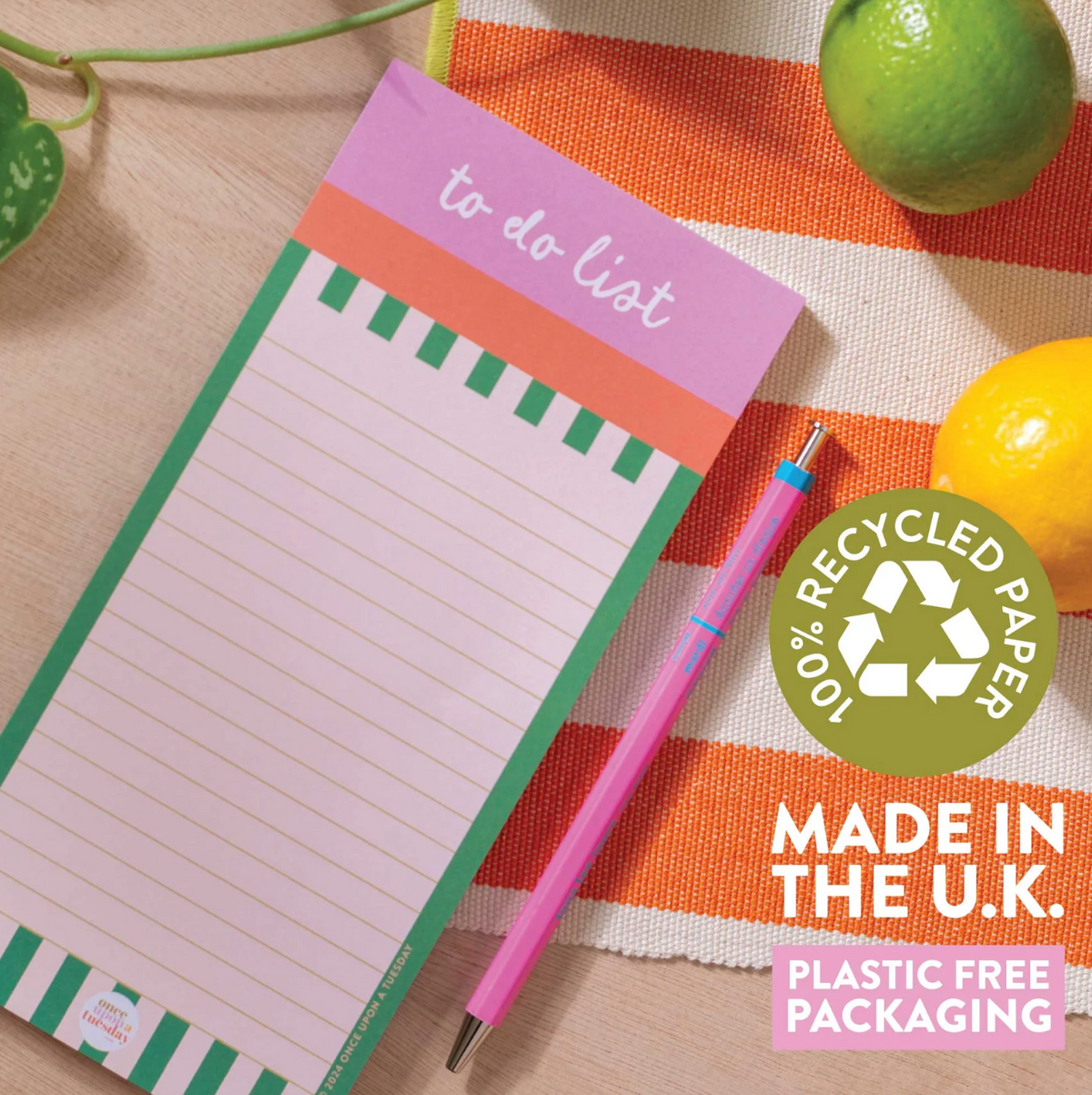 A pastel to-do list notepad with a pink header, orange and green striped border, shown on a striped fabric surface with a pink pen, limes, and a lemon. A circular badge reads '10% recycled paper' and 'Made in the UK.
