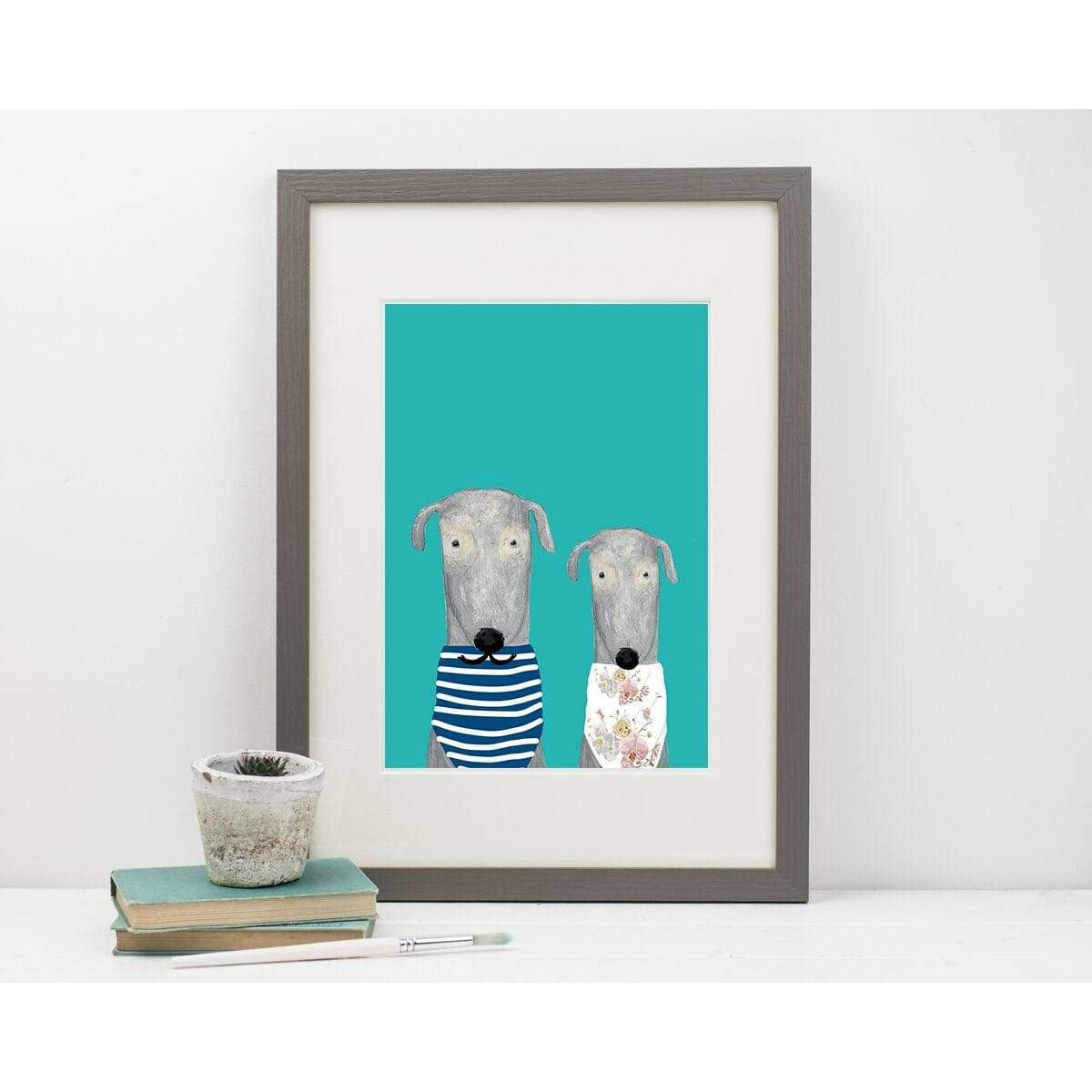 Framed artwork of two dogs on a teal background, displayed on a white surface