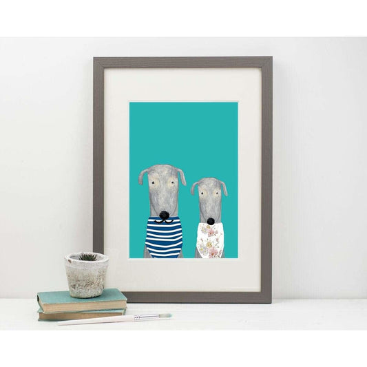 Framed artwork of two dogs on a teal background, displayed on a white surface
