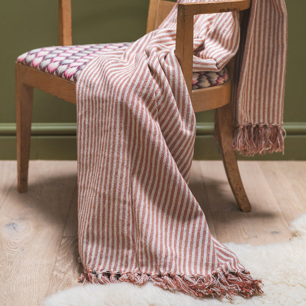 Wooden chair with a striped red and white throw draped over it against a green wall.
