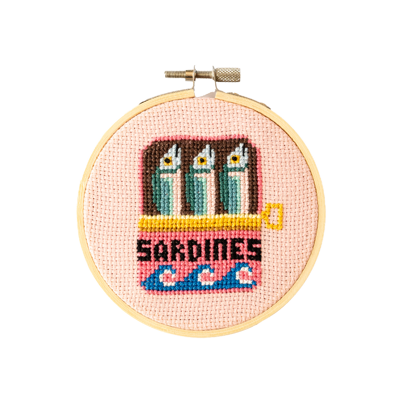 Cross-stitched design of sardines in a can on a pink background