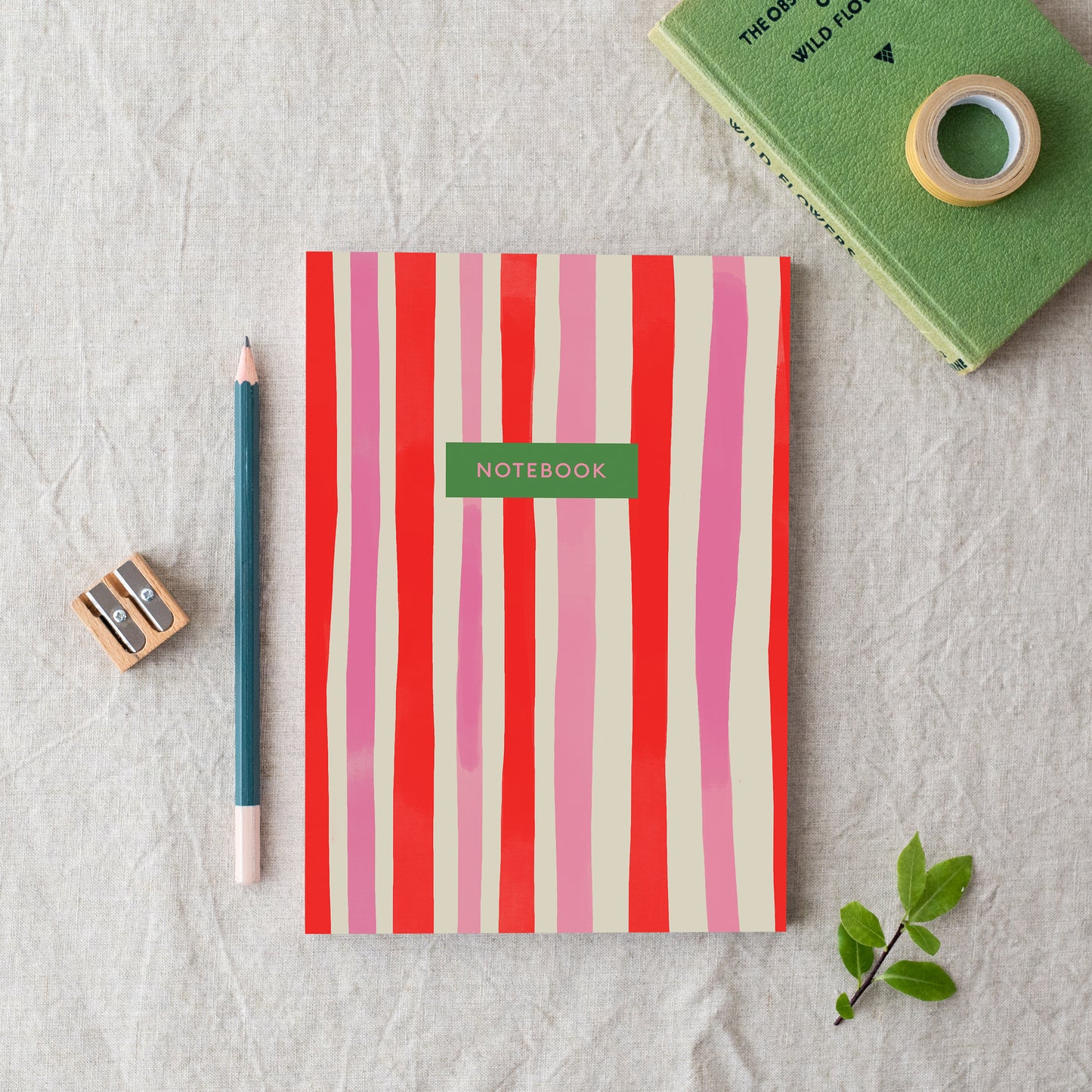 An A5 notebook with red and pink vertical stripes, labelled 'notebook', made in Britain from bleed proof, eco-friendly, recycled paper with 100gsm inner pages.