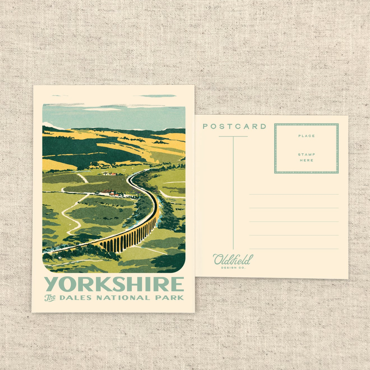 A vintage-style postcard set featuring an illustrated landscape of Yorkshire Dales National Park, shown on a textured beige fabric background. One postcard displays the scenic front with the text 'YORKSHIRE' and 'DALES NATIONAL PARK,' while the other shows the back with postcard fields and a signature reading 'Oldfield Design Co.