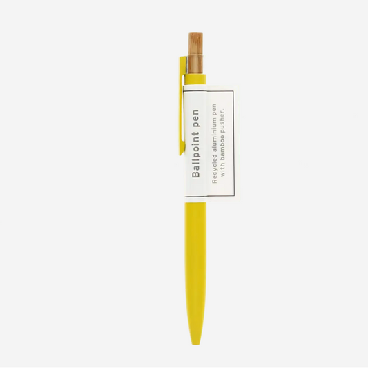 A yellow ballpoint pen with a bamboo clip and a white paper label wrapped around the middle, shown against a light gray background.